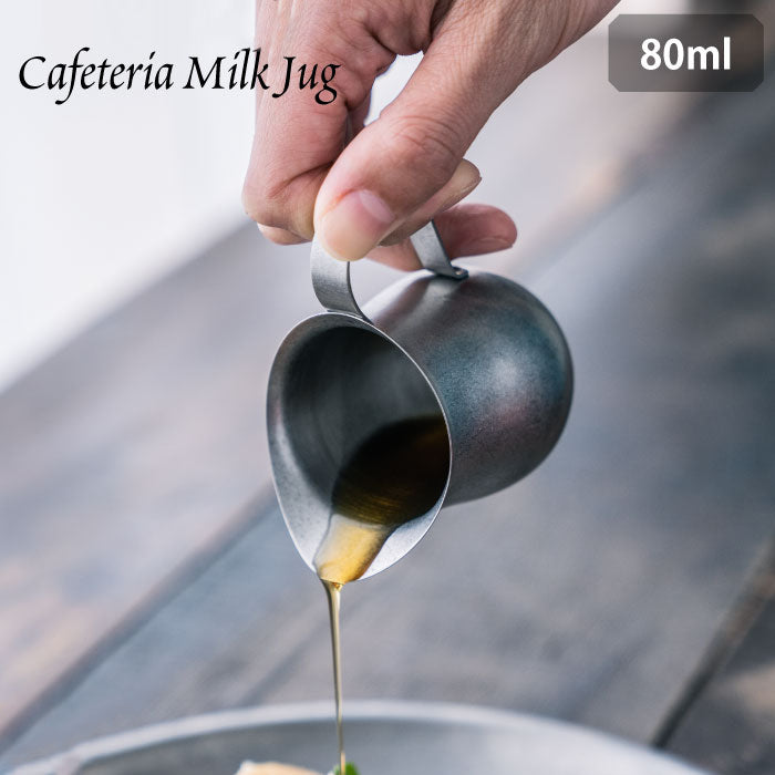 Hand pouring liquid from VINTAGE INOX 80ml stainless steel cafeteria milk jug.