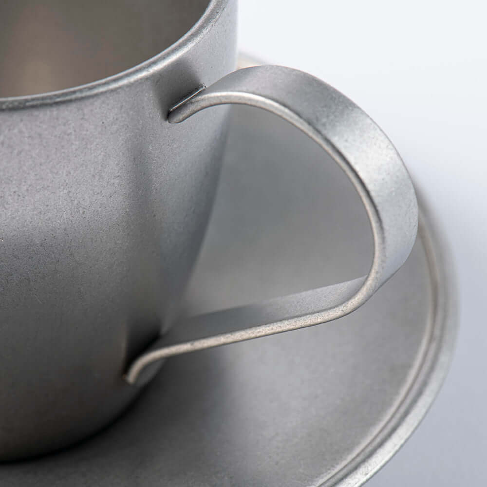 Close-up of a vintage inox stainless steel cup with a handle and matching saucer, showcasing elegant craftsmanship and design.
