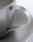 Close-up of a vintage inox stainless steel cup with a handle and matching saucer, showcasing elegant craftsmanship and design.