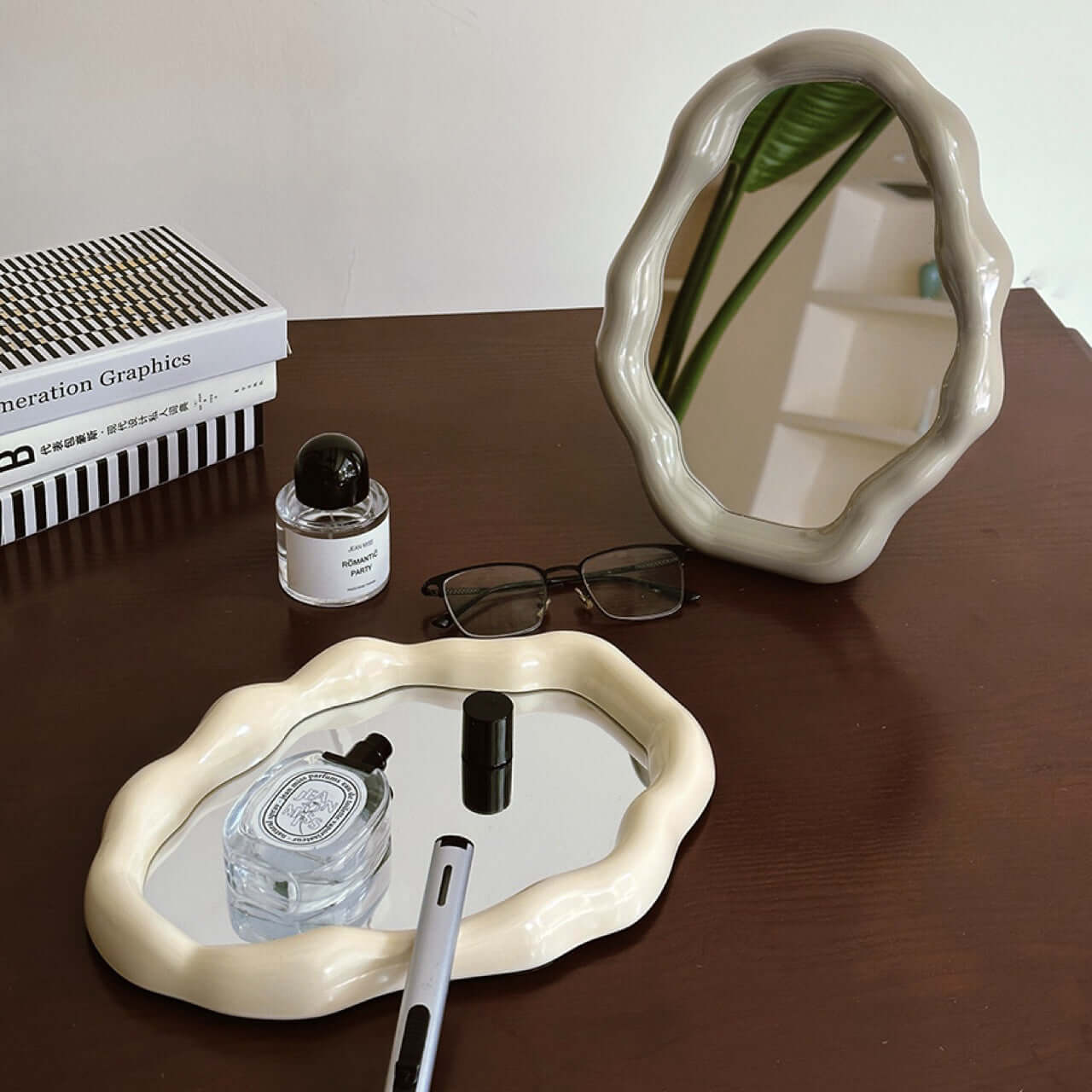 Nordic cloud-shaped vanity mirror on a wooden table with decor items including a book, glasses, and perfume bottle.