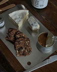Minimalist stainless steel cutting board used as serving platter with cheese, crackers, and spread on wooden table.