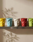 Crushed Ceramic Mugs in five colours on a steel shelf with the Orbit clock