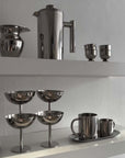 Stainless steel kitchenware set including mugs, cups, and a teapot with a sleek modern design on display shelves