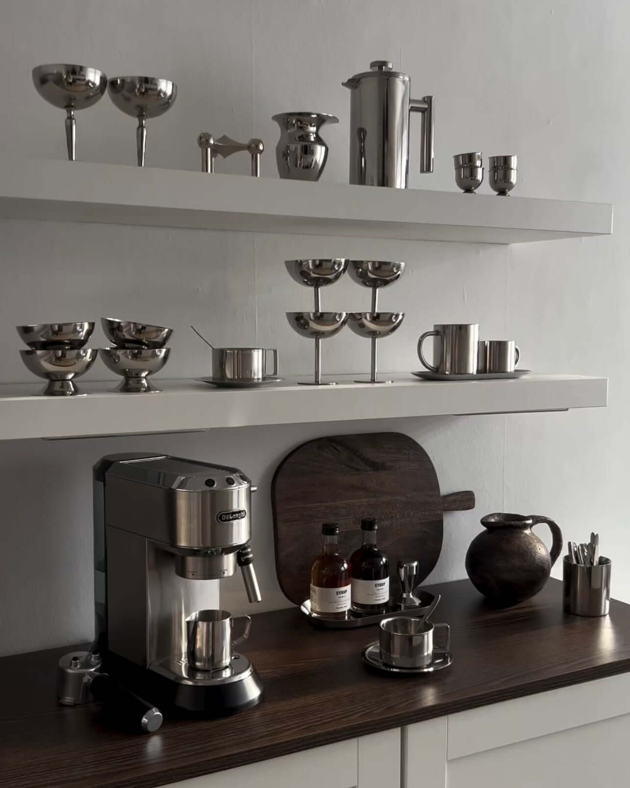 Modern kitchen countertop with stainless steel appliances, espresso machine, and elegant drinkware on white shelves