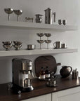 Modern kitchen countertop with stainless steel appliances, espresso machine, and elegant drinkware on white shelves