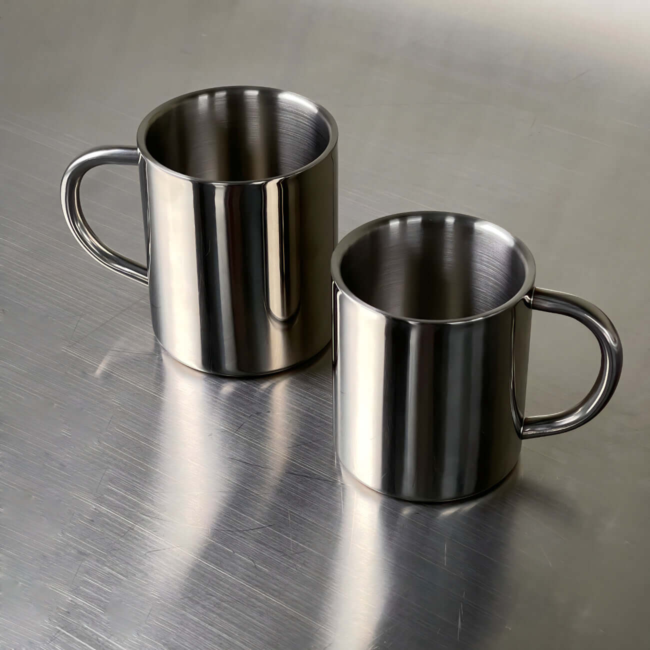 Double-layer glossy stainless steel cups on metallic surface, modern elegance for temperature control and versatile use.