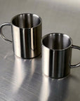 Double-layer glossy stainless steel cups on metallic surface, modern elegance for temperature control and versatile use.