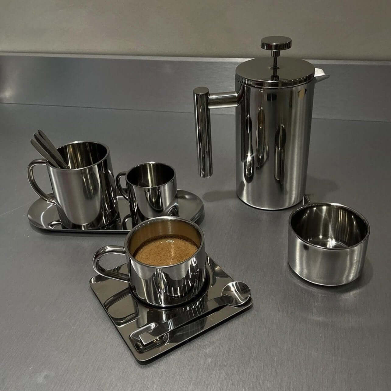 Stainless steel French press coffee pot and cups on a table, showcasing sleek design and double-layer insulation.