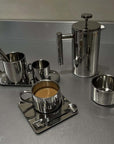 Stainless steel French press coffee pot and cups on a table, showcasing sleek design and double-layer insulation.