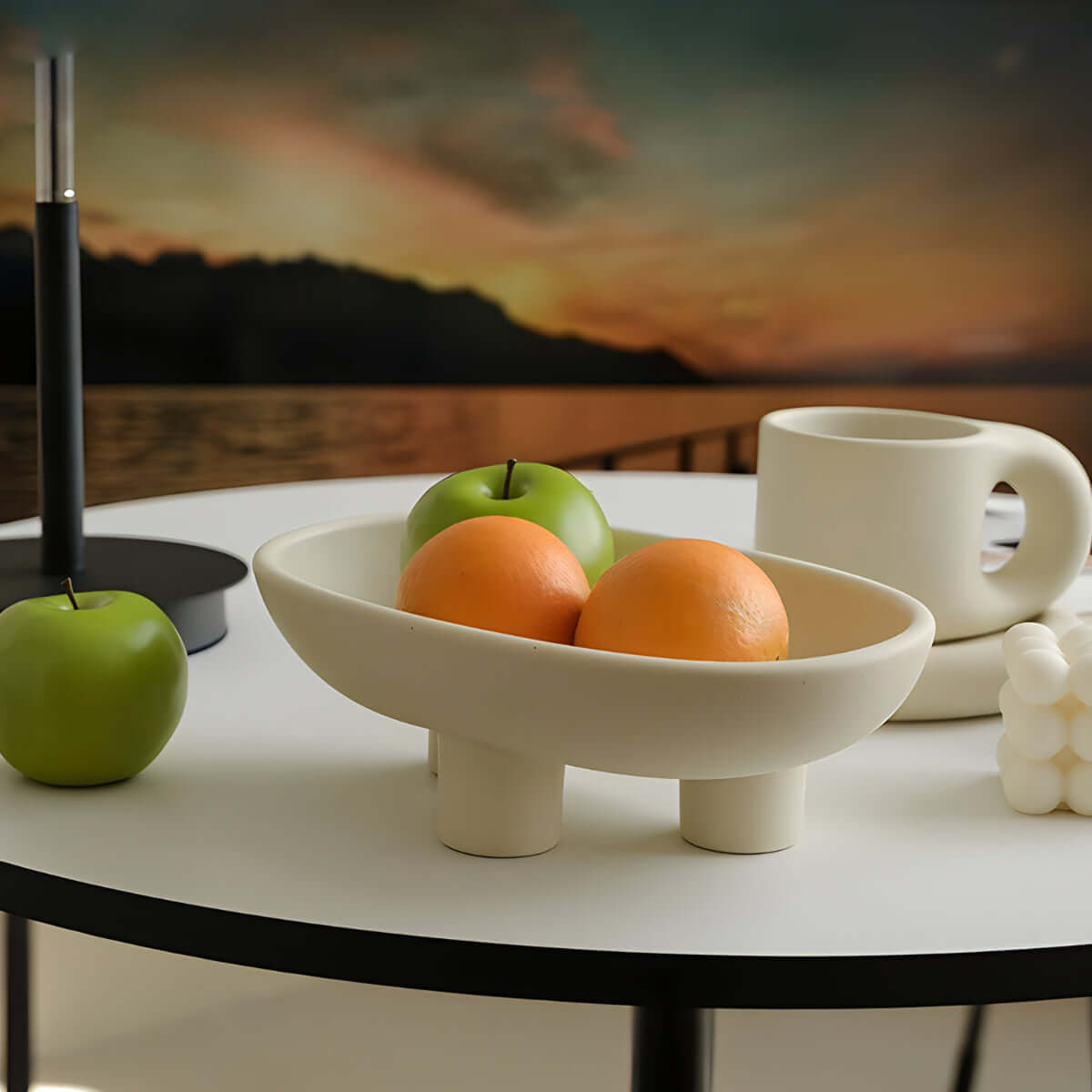 Elegant ceramic three-legged fruit and snack plate with apples and oranges, enhancing a sophisticated dining table setting.