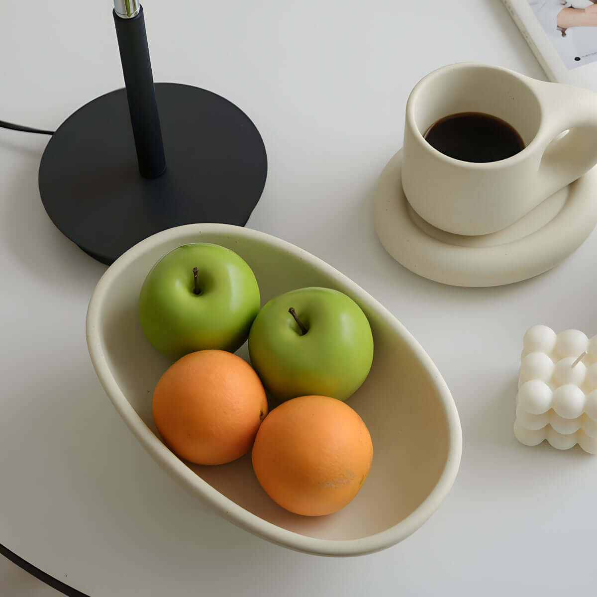 Elegant ceramic fruit plate with apples and oranges beside a stylish mug on a minimalist dining table setting.