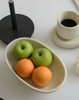 Elegant ceramic fruit plate with apples and oranges beside a stylish mug on a minimalist dining table setting.