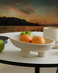 Elegant ceramic three-legged fruit and snack plate with apples and oranges, enhancing a sophisticated dining table setting.
