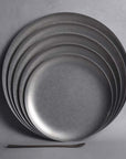 Stack of Hakone Plates in matte-finished stainless steel, showcasing minimalist design and elegant curves for dining.