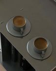 Two VINTAGE INOX stainless steel cups and saucers with espresso, chic design, on a grey tabletop.