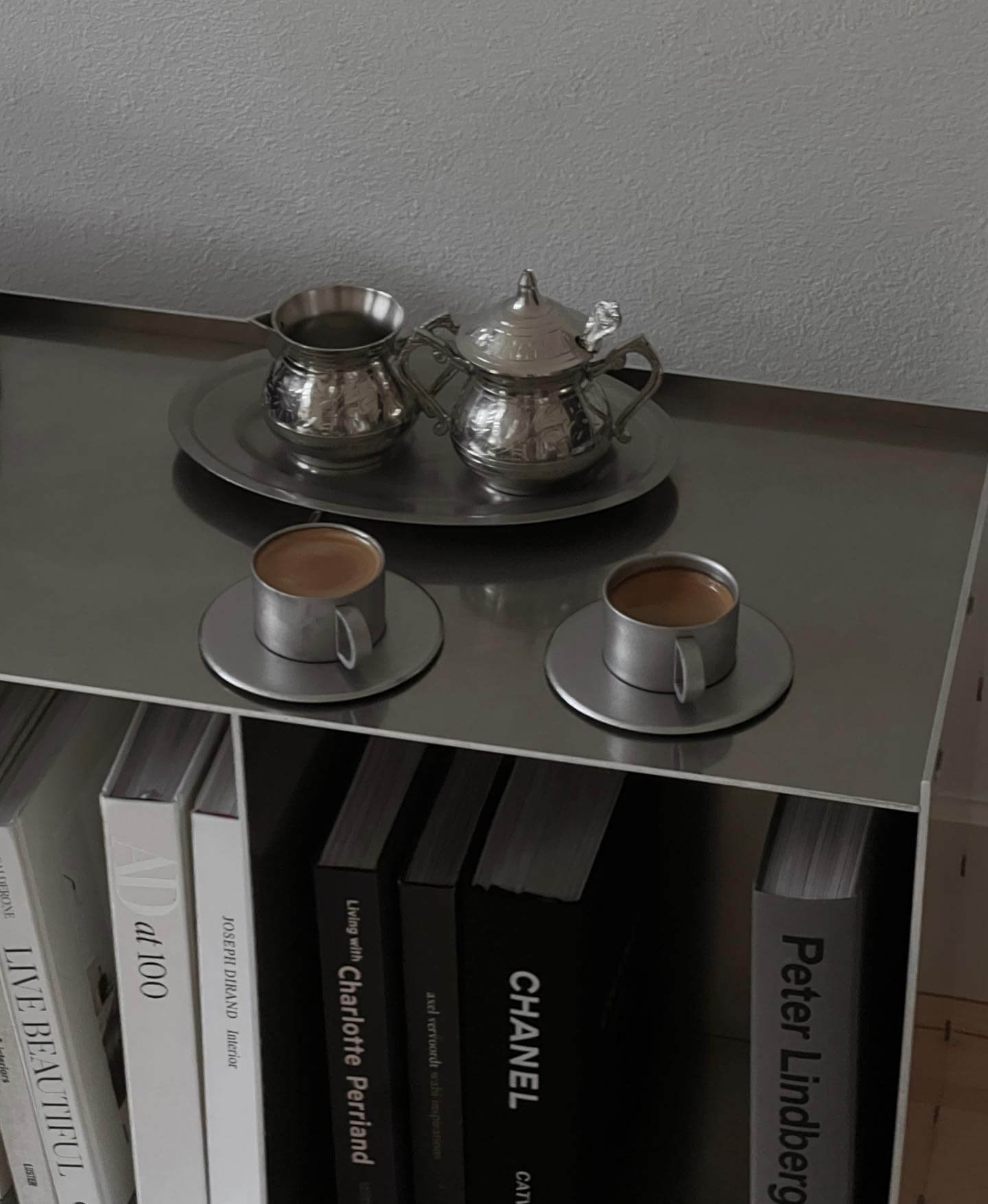 Vintage INOX stainless steel cup and saucer set with teapot and creamer on a shelf with books.