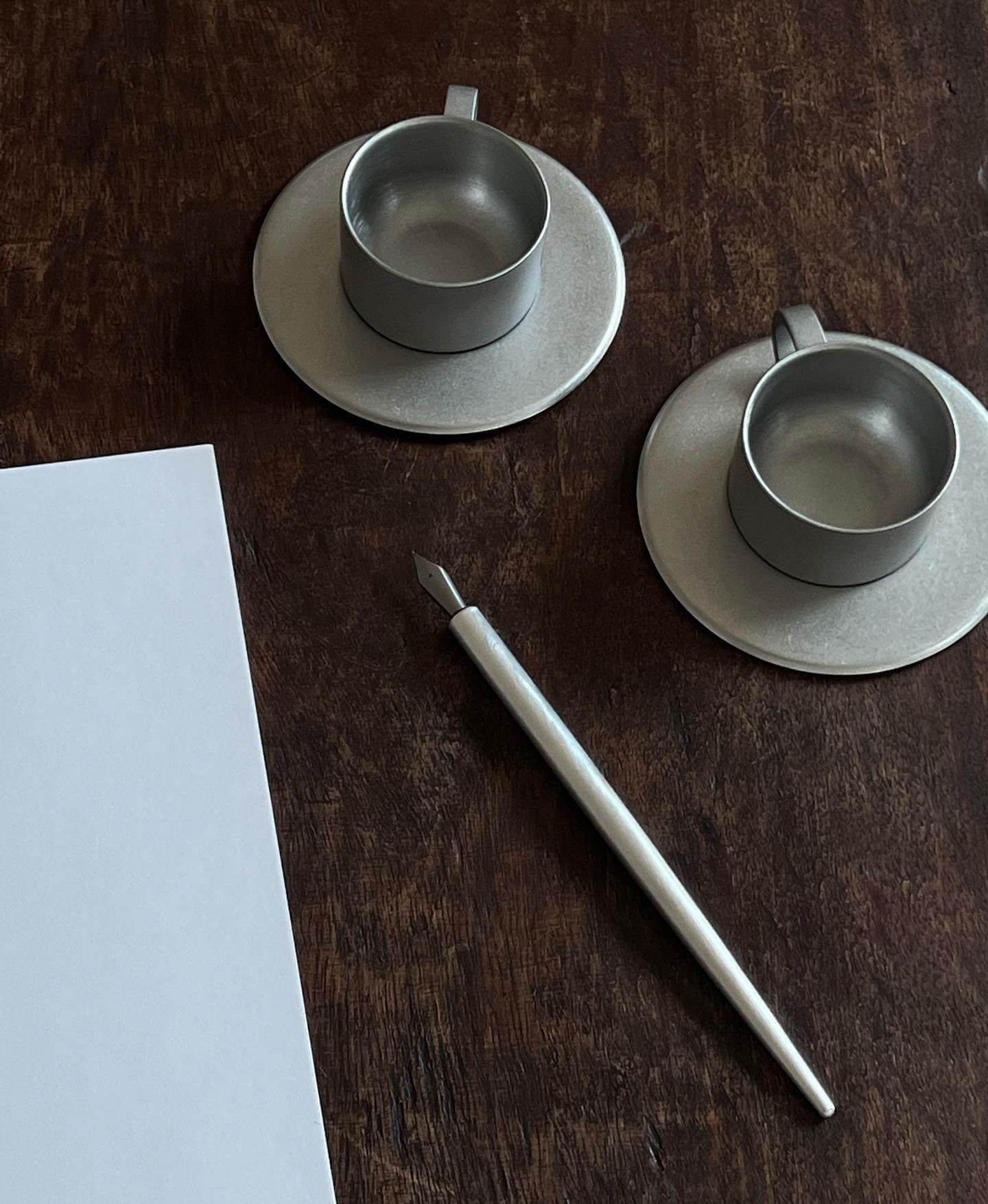 Stainless steel vintage cup and saucer set with pen on wooden table, showcasing elegant design and durability.