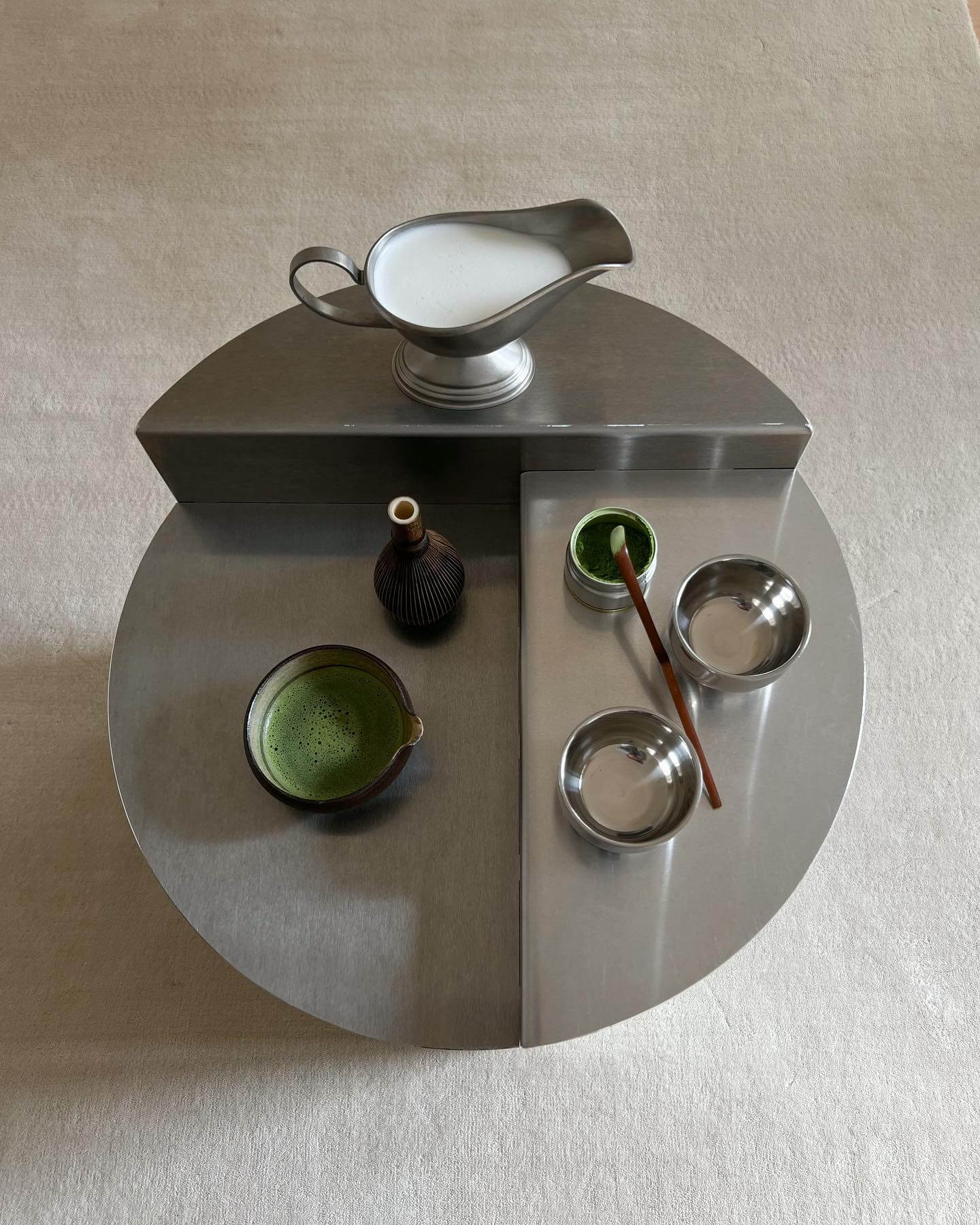 Modern tea set with stainless steel pitcher and bowls on a sleek circular table showcasing stylish design and functionality.