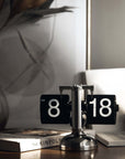 Stylish turning desktop clock with a page-turning mechanism, ideal for Japanese or Nordic-inspired interiors, on a wooden desk.