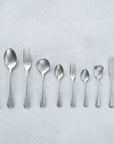 Vintage Inox Old English Series cutlery set with simple smooth handles, featuring knife, spoons, and forks on a textured background.