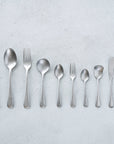 Vintage Inox Old English Series cutlery set with simple smooth handles, featuring knife, spoons, and forks on a textured background.