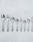 Vintage Inox Old English Series cutlery set with simple smooth handles, featuring knife, spoons, and forks on a textured background.