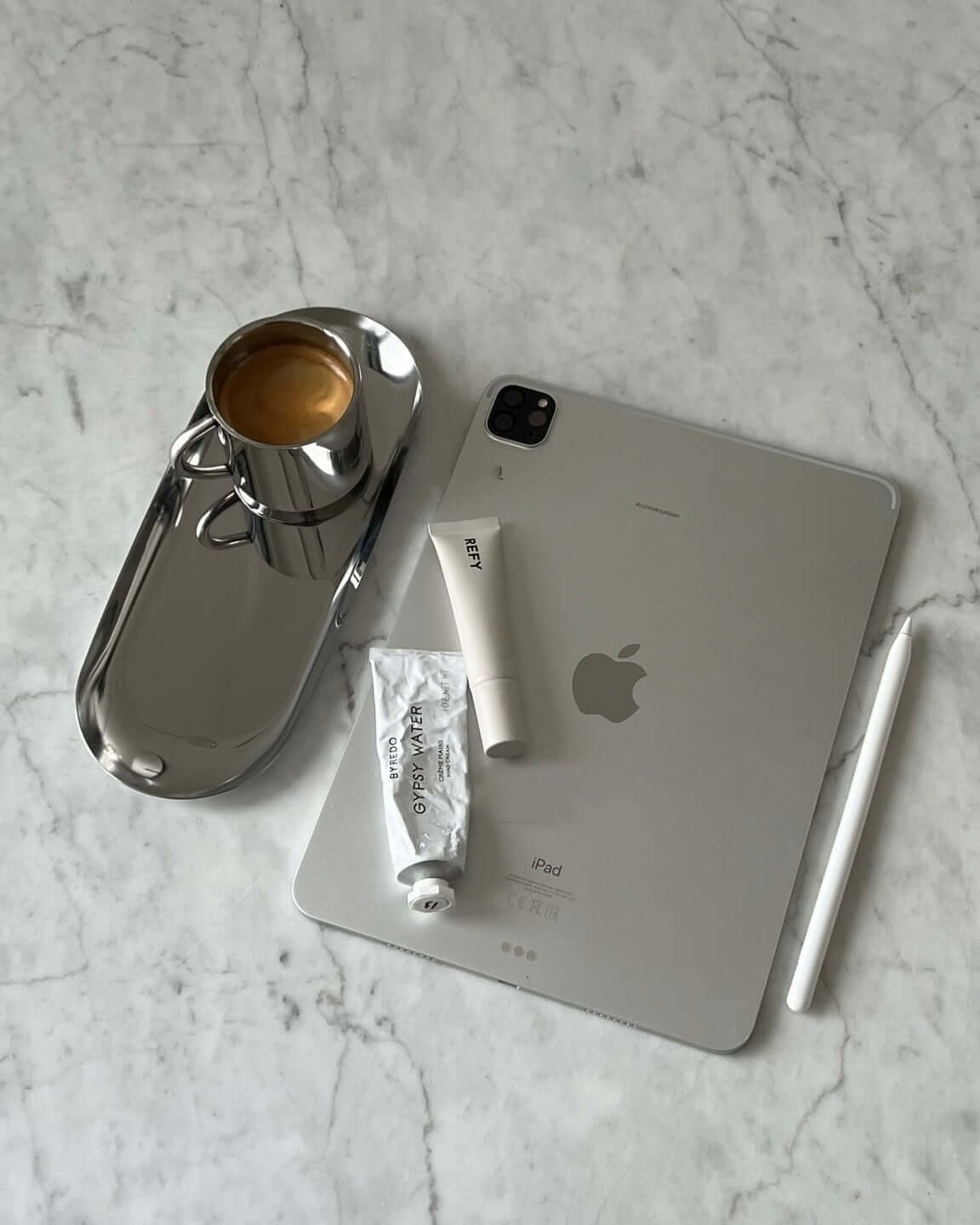 Minimalist steel tray with coffee cup next to tablet and stationery on marble surface.