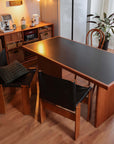 Cherry wood Gora dining table with black leather Nosaku monk chairs in cozy room setting.