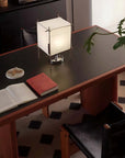 Elegant dining table setup with modern lamp, open book, and plant decor on a sleek dark surface.