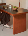 Elegant cherry wood dining table with a dark top, styled with a bowl of green grapes, minimal decor, and a cozy brown chair.