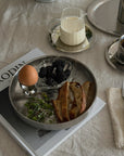 Noir Steel Plate with breakfast beside a steel French press and candle