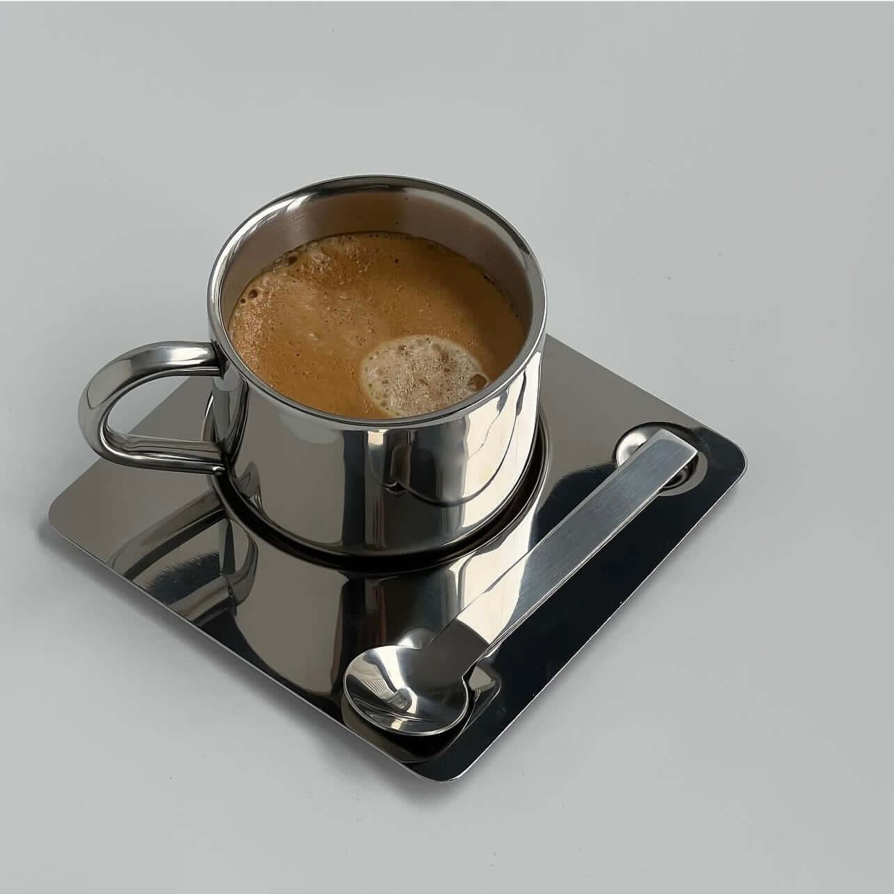 Stainless steel espresso cup on a sleek metal saucer with spoon, part of the Limited Steel Bundle coffee set.
