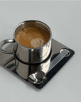Stainless steel espresso cup on a sleek metal saucer with spoon, part of the Limited Steel Bundle coffee set.
