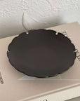 Black Yukiwa Plate by Yoshida Pottery on a beige book, showcasing intricate nature-inspired design and elegant craftsmanship.