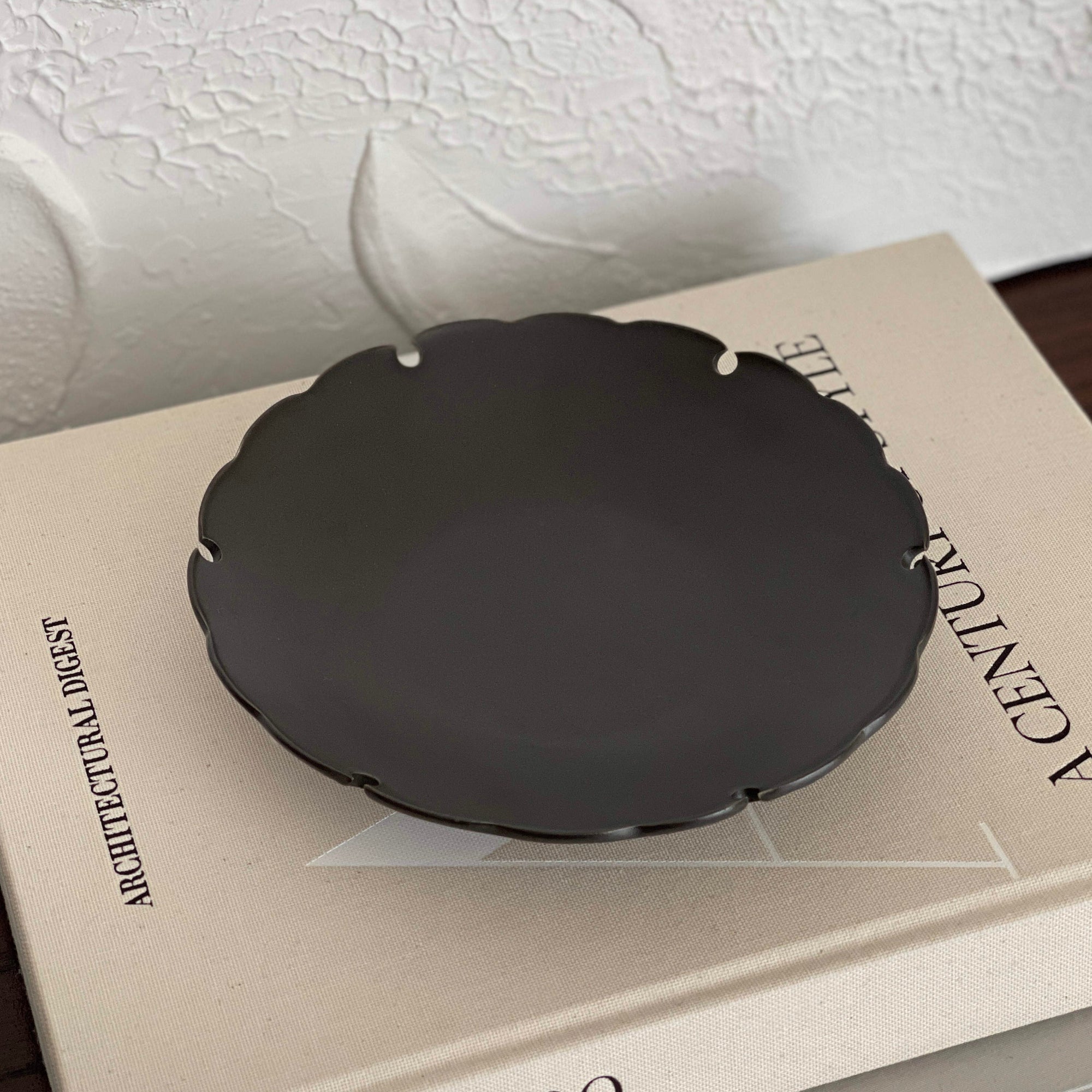 Black Yukiwa Plate by Yoshida Pottery on a beige book, showcasing intricate nature-inspired design and elegant craftsmanship.