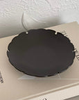Black Yukiwa Plate by Yoshida Pottery on a beige book, showcasing intricate nature-inspired design and elegant craftsmanship.