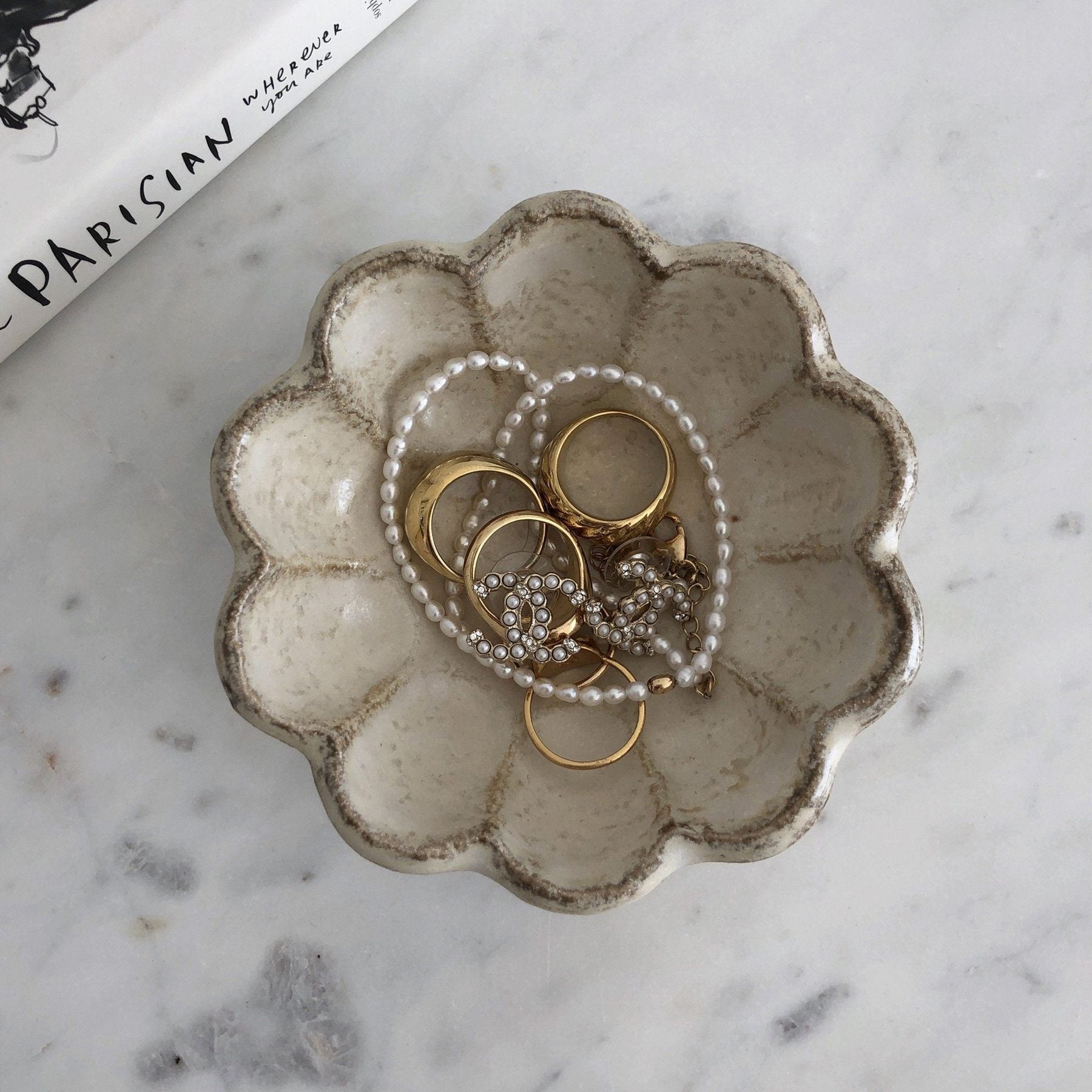 Decorative porcelain dish with jewelry and pearl necklace on marble surface.