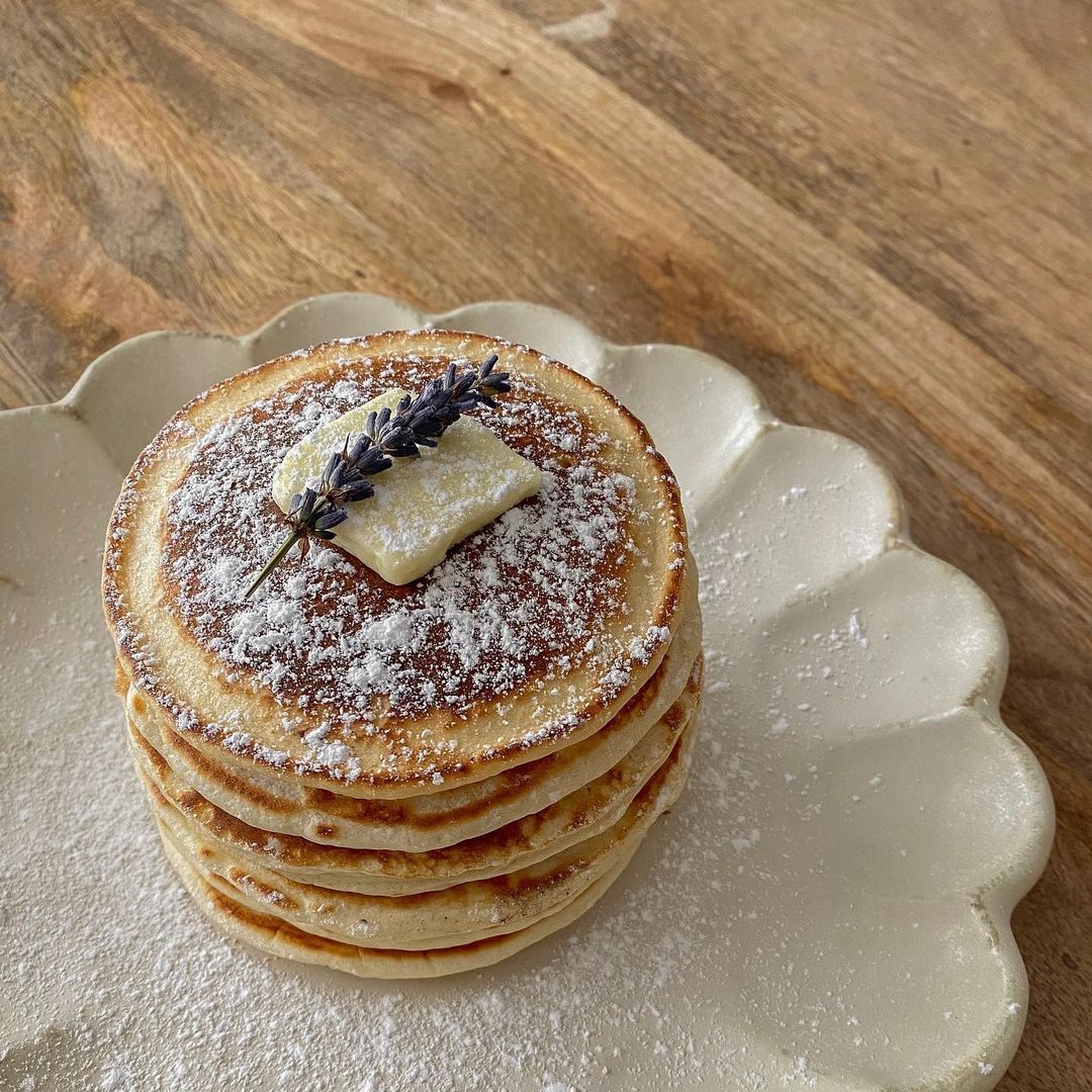 Stack of pancakes with butter and lavender on a scalloped Rinka plate, showcasing elegant Japanese porcelain craftsmanship.