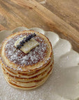 Stack of pancakes with butter and lavender on a scalloped Rinka plate, showcasing elegant Japanese porcelain craftsmanship.