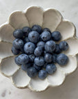 Porcelain flower-shaped bowl filled with fresh blueberries on a marble surface.
