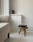 Minimalist living room with cozy textured sofa, wooden stool, and decorative bowl on a white floor.