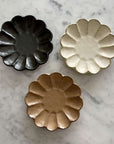 Three decorative flower-shaped porcelain plates in black, cream, and bronze colors, arranged on a marble surface.