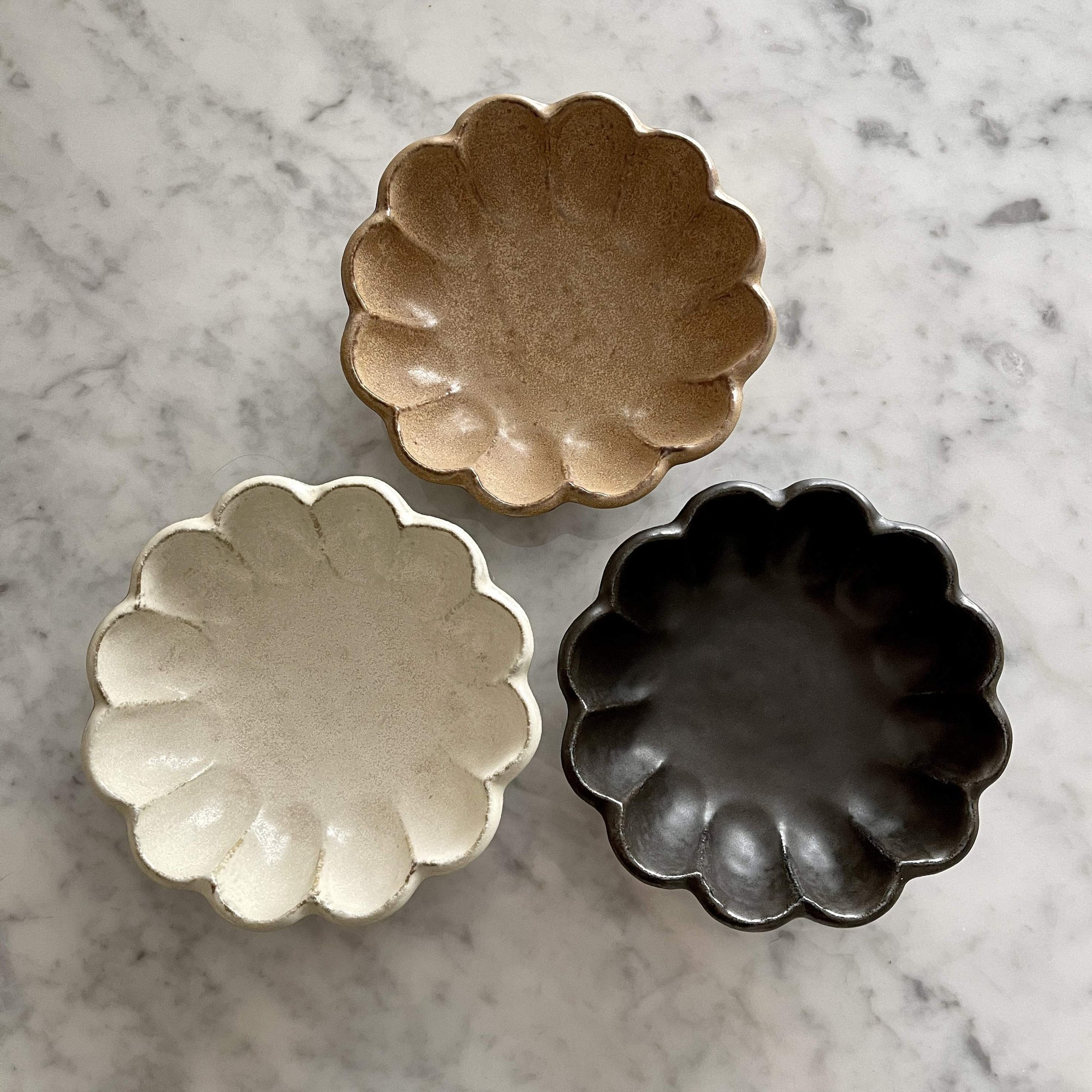 Three Rinka Collection bowls by Kaneko Kohyo in brown, white, and black porcelain on a marble surface.