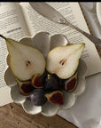 Sliced pear and figs in a scalloped ceramic bowl beside an open book with a vintage knife on a wooden surface.