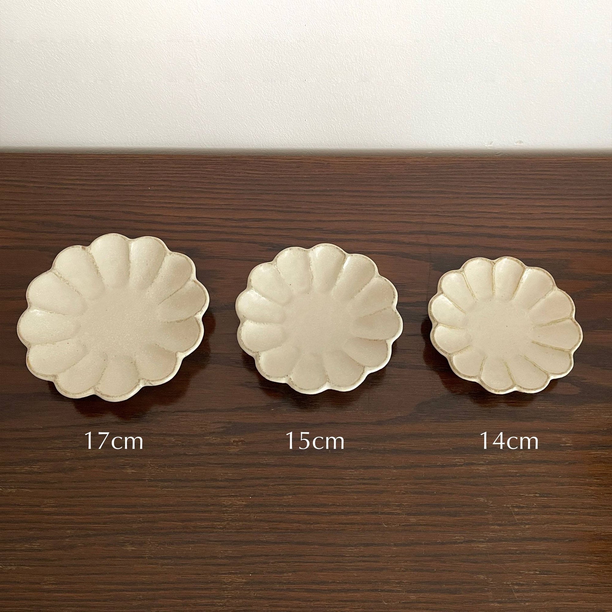 Three Rinka plates in sizes 17cm, 15cm, and 14cm displayed on a wooden table, featuring delicate scalloped edges.