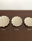 Three Rinka plates in sizes 17cm, 15cm, and 14cm displayed on a wooden table, featuring delicate scalloped edges.
