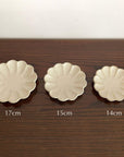 Three Rinka plates in sizes 17cm, 15cm, and 14cm displayed on a wooden table, featuring delicate scalloped edges.