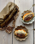 Two Rinka bowls by Kaneko Kohyo with desserts beside a gold chain brown bag on a wooden surface.
