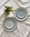 Two Storia Plates 24cm on white cloth, featuring antique-inspired lace edges and flecked lacquer finish beside a bouquet of flowers.