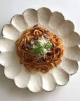 White porcelain Rinka plate with spaghetti topped with basil, representing Kaneko Kohyo's handcrafted Rinka Collection.